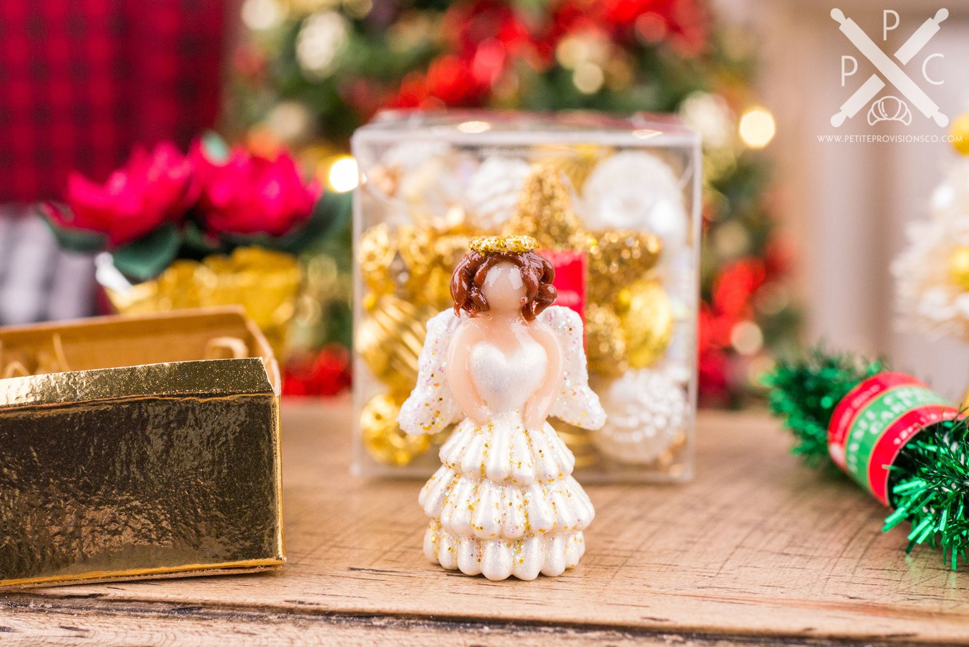 Miniature Christmas angel tree topper in a white and gold dress surrounded by festive ornaments and holiday decorations.