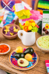 A dollhouse miniature replica of a Mexican meal. The plate is filled with avocados, onions, and other realistic food items.