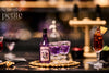 A bottle of Belladonna Nightshade Cordial and two small glasses filled with purple liquid on a gold tray.