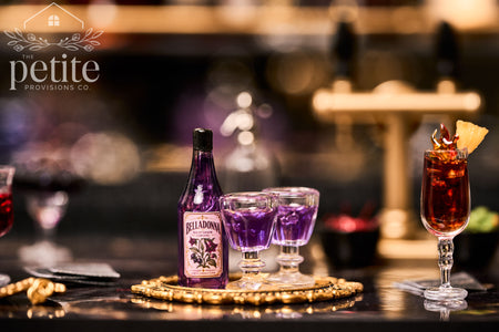 A bottle of Belladonna Nightshade Cordial and two small glasses filled with purple liquid on a gold tray.