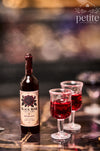 Handcrafted 1:12 scale Black Rose Cellars Merlot miniature wine bottle with a vintage rose label beside two stemmed glasses filled with deep ruby-red resin wine.