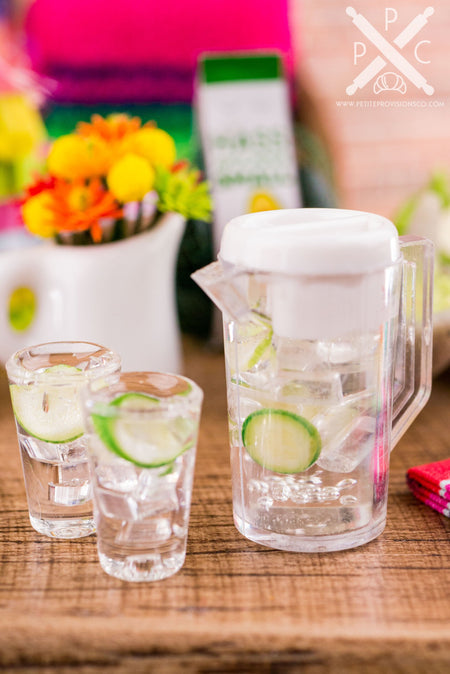 A handmade dollhouse miniature replica of a pitcher of ice water with cucumber slices and two matching glasses.