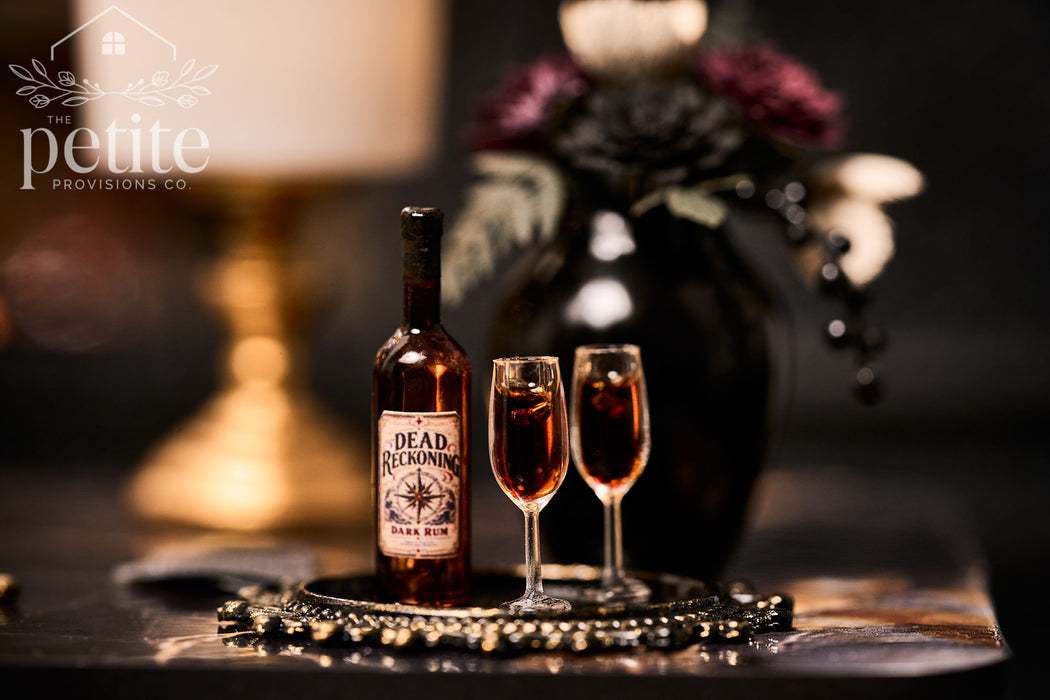 Handcrafted 1:12 scale Dead Reckoning Dark Rum Service featuring an amber rum bottle and two filled stemmed glasses on an ornate black and antique-gold tray.