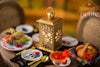 Handcrafted 1:12 scale Día de los Muertos lantern with gold sugar skull and floral cutouts, surrounded by miniature tamales, pan de muerto, decorative plates, and a marigold margarita.