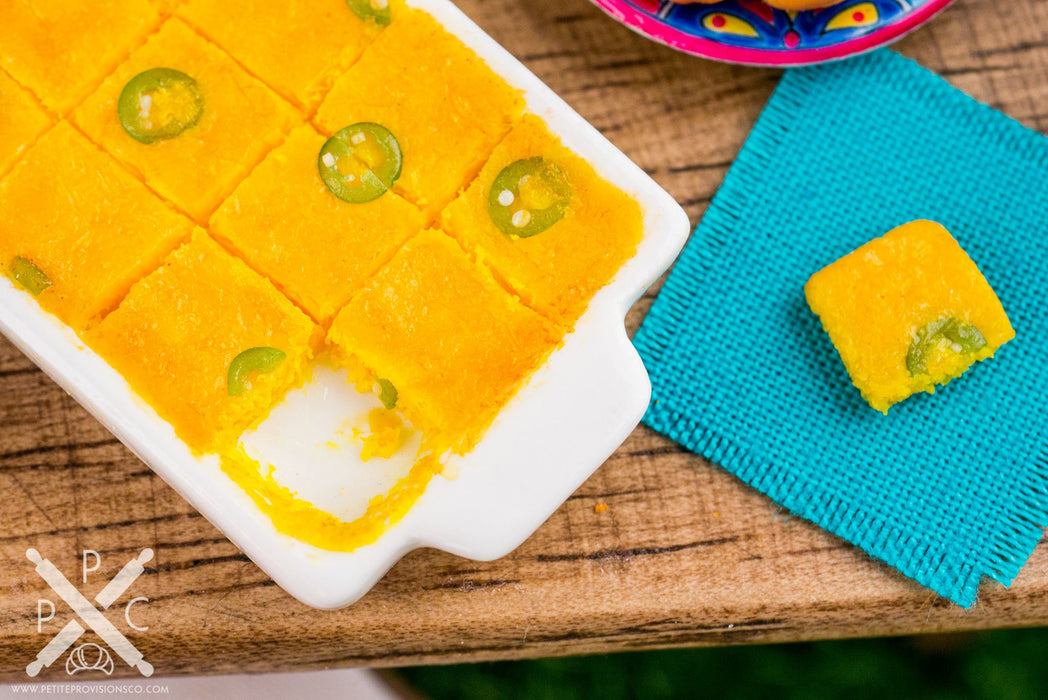 A close-up of a dollhouse miniature replica of a freshly baked jalapeño cornbread square. The cornbread is moist and fluffy, with a hint of spice from the jalapeños.