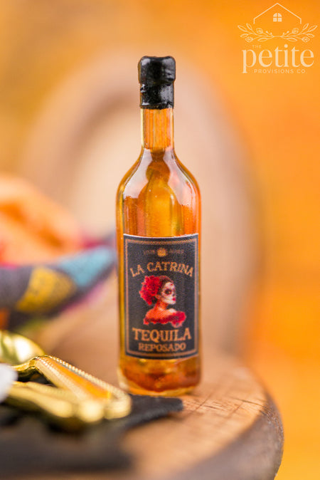 Handcrafted 1:12 scale La Catrina Tequila Reposado miniature bottle with amber resin, black-and-gold Día de los Muertos label, and black bottle cap.