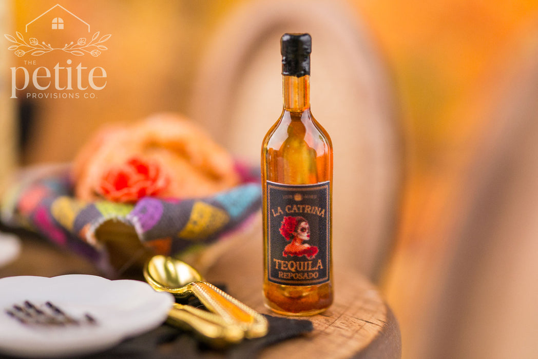 Miniature La Catrina Tequila Reposado bottle displayed on a rustic wooden table with gold silverware, colorful Día de los Muertos decorations, and a warm autumn background.