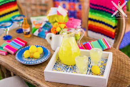 A miniature dollhouse replica of a glass pitcher of lemonade, with two glasses and a lemon on a tray.