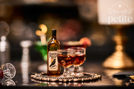 Handcrafted 1:12 scale Raven's Keep Bourbon Whiskey Service with an amber bottle featuring a raven label and two filled whiskey glasses on an ornate antique-gold tray.