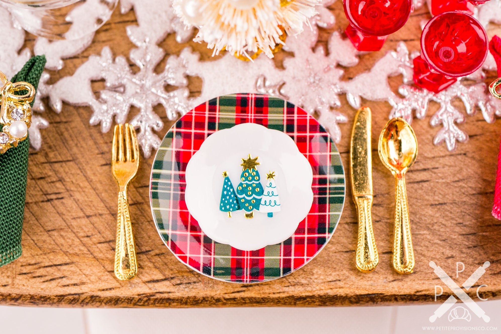Miniature Christmas place setting with plaid dinner plate, Christmas tree accent plate, gold flatware, and festive decorations.