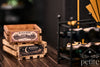Two handcrafted 1:12 scale miniature wooden wine crates with vintage Black Rose Cellars and Moonfall Estate vineyard labels, stacked beside a miniature wine rack.