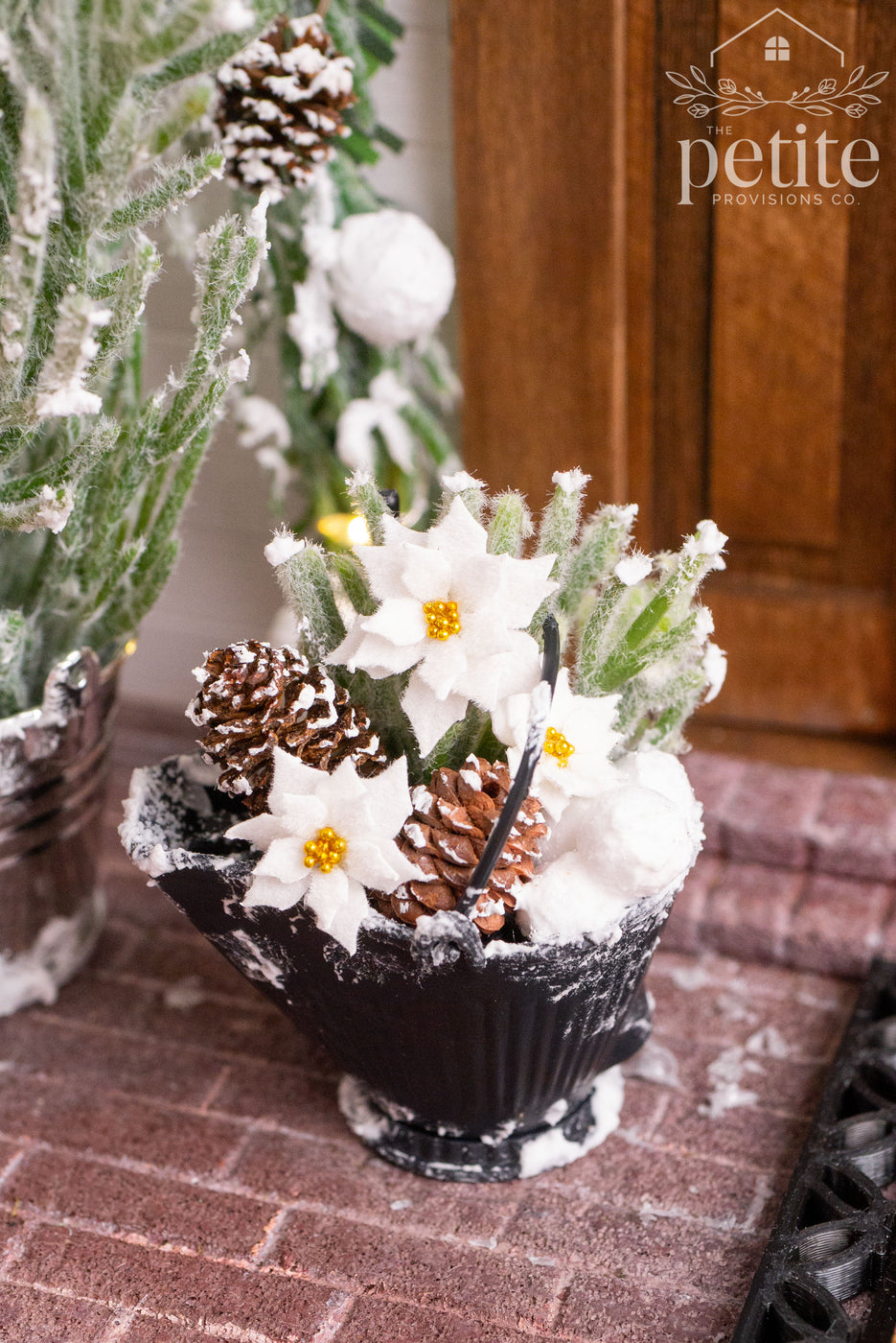 Snowy miniature coal scuttle arrangement filled with frosted greenery, pinecones, and white poinsettias.